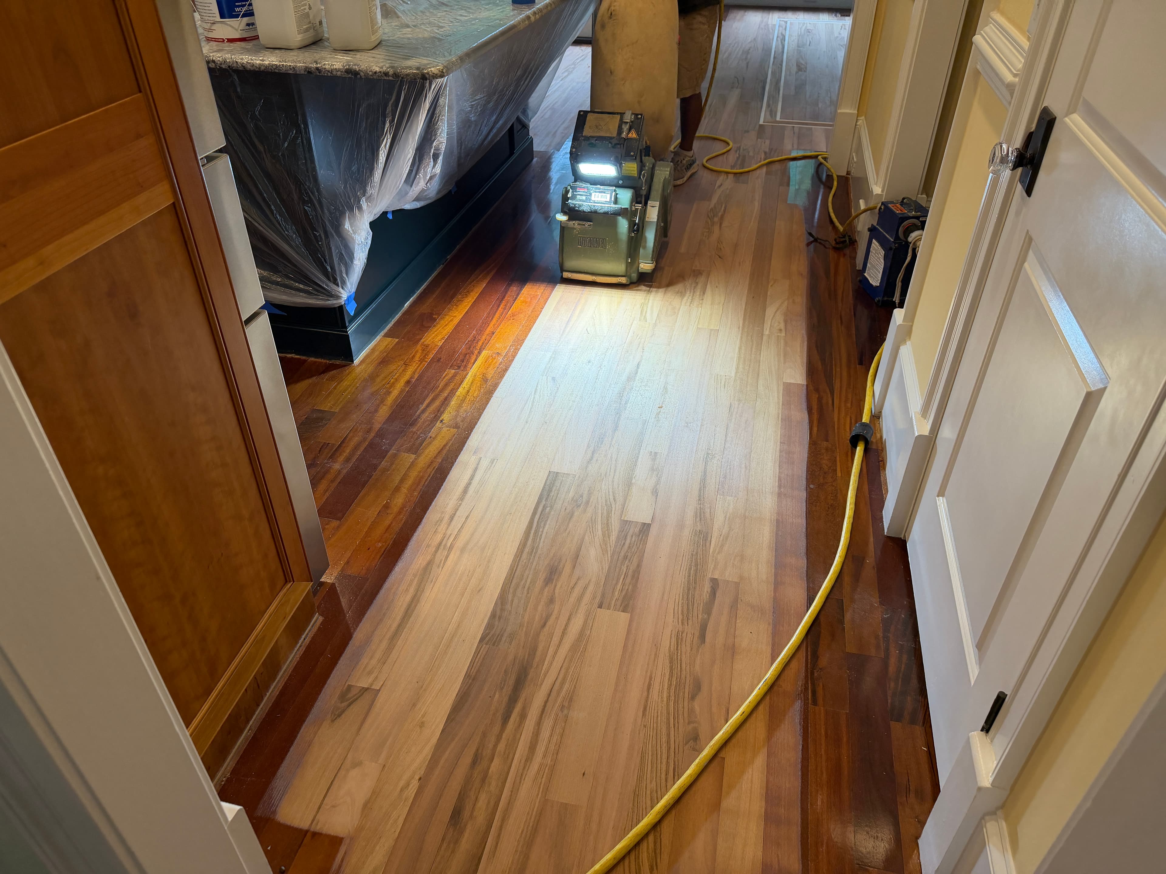 Hardwood floor sanding in progress mid-job showing bare wood pass lane alongside existing finish